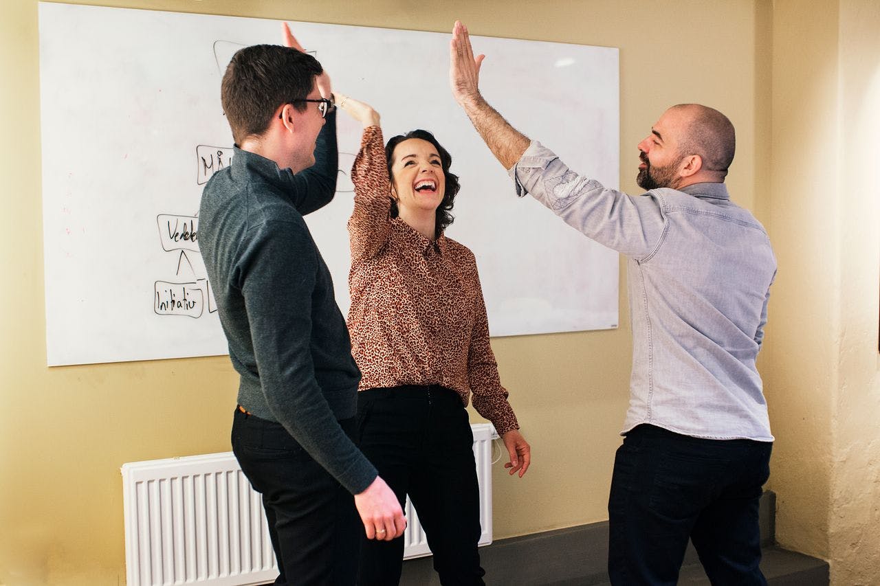 Tre personer som koser seg med samarbeid og feirer det med en mer eller mindre vellykket high five.