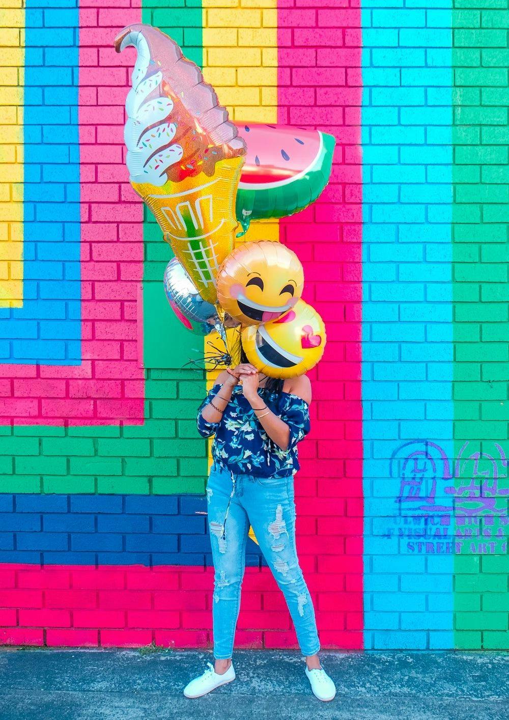 Kvinne i fargerike omgivelser som skjuler ansiktet med smilende ballonger
